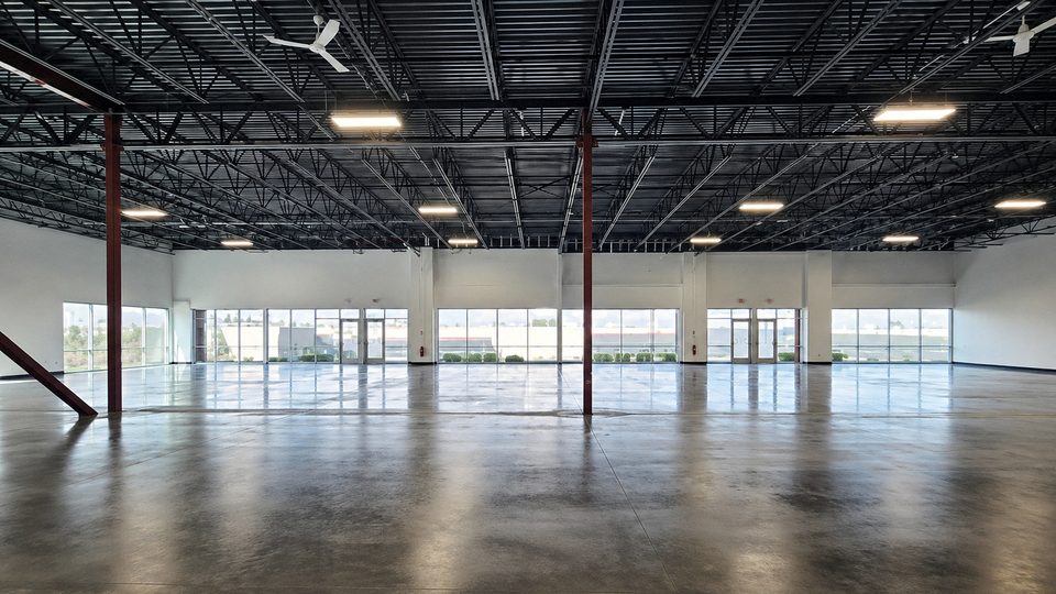 The empty Fathom North space in Oak Creek — sealed concrete floor, exposed steel ceiling, and a full wall of windows, photographed before buildout